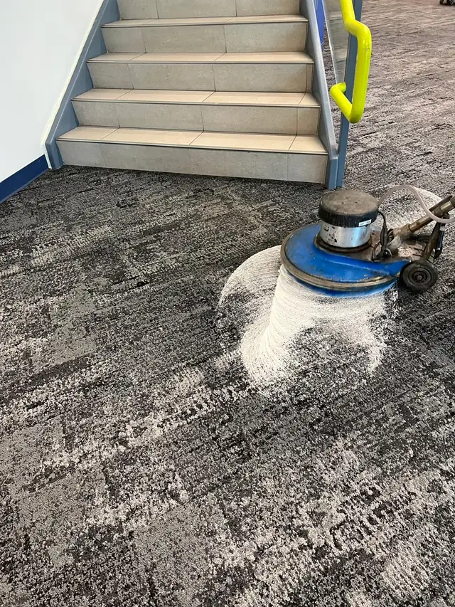 A rotary cleaning machine working on patterned carpet beside a stairway